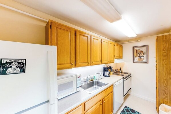 A compact kitchen with wooden cabinets, a white refrigerator, a microwave, a sink, and a stove.