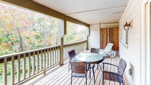 A covered outdoor area with a wooden deck, a round table with chairs, and a view of trees.