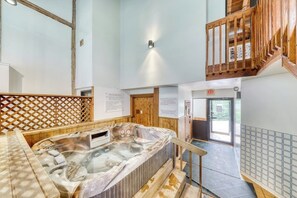 A hot tub in a room with wooden walls, a wooden staircase, and an exit sign.