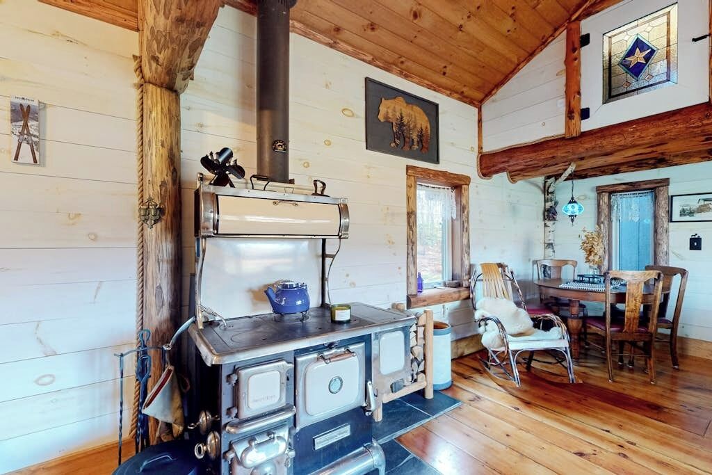 L’intérieur d’un chalet rustique, avec un poêle à bois, des murs en bois, un coin repas avec des chaises et une œuvre d’art sur le thème des ours.