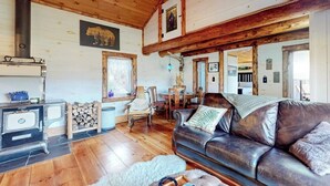 A cozy cabin interior with a wooden ceiling, a fireplace, a leather sofa, and a dining area. - Renovated historic cabin with mountain views, lake access, & electric fireplace (Jay)