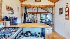 A cabin interior with a kitchen area featuring a stove, a dining table, and a sofa. - Renovated historic cabin with mountain views, lake access, & electric fireplace (Jay)