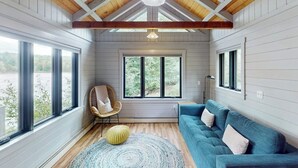 Une pièce avec un canapé bleu, un fauteuil, un tapis rond et de grandes fenêtres donnant sur un beau paysage.