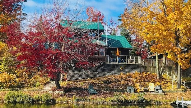 Un chalet au bord du lac, doté d’un toit végétalisé, entouré d’un paysage automnal aux couleurs flamboyantes.