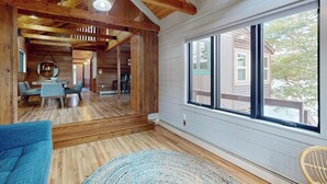 Une pièce spacieuse avec des poutres en bois, une grande fenêtre et une vue sur une maison à l’extérieur.