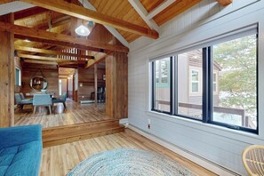 Ein geräumiger Raum mit Holzbalken, einem großen Fenster und Blick auf ein Haus außerhalb.