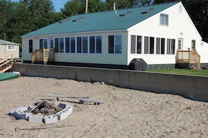 A single-story house with a green roof, large windows, and a deck. - Lakeside cottage w/ mountain views, canoes, firepit, enclosed porch, bbq, beach (Colchester)