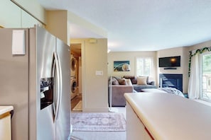 A modern kitchen with a built-in refrigerator, a dining area with a table, a sofa, and a TV mounted on the wall. - Cozy Ski-in/Ski-out condo w/ balcony, mountain views, gas fireplace, w/d, wifi (Jay)
