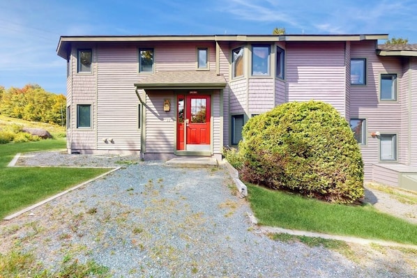 A two-story building with a red door, a small porch, and a well-maintained lawn. - Cozy Ski-in/Ski-out condo w/ balcony, mountain views, gas fireplace, w/d, wifi (Jay)