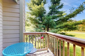 A wooden deck with a blue chair, a metal railing, and a view of a large tree and grassy area. - Cozy Ski-in/Ski-out condo w/ balcony, mountain views, gas fireplace, w/d, wifi (Jay)