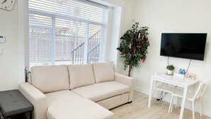 A living room with a sofa, a small table, a TV, and a plant. - *AC/8mins-YVR/Private Bathroom Suite/Separate Entry/Free Parking/Near Skytrain (Richmond)