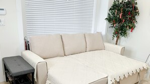 A beige sofa with a quilted cover, a small black stool, and a potted plant with red decorations. - *AC/8mins-YVR/Private Bathroom Suite/Separate Entry/Free Parking/Near Skytrain (Richmond)