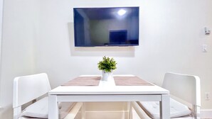 A modern room with a white table, two white chairs, a flat-screen TV mounted on the wall, and a small potted plant on the table. - *AC/8mins-YVR/Private Bathroom Suite/Separate Entry/Free Parking/Near Skytrain (Richmond)