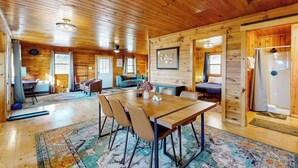 A wooden cabin interior with a dining area, a sofa, a bed, and a refrigerator. - Cozy house w/ mountain views, large yard, firepit, wifi, jetted tub, TV, EV (Glover)