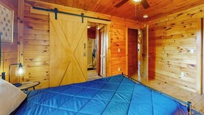 A wooden cabin interior with a bed, a ceiling fan, and a sliding door. - Cozy house w/ mountain views, large yard, firepit, wifi, jetted tub, TV, EV (Glover)