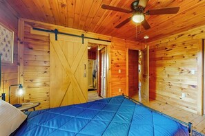 Interior de una cabaña de madera con cama, ventilador de techo y puerta corrediza.