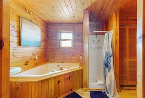 Un baño de cabaña de madera con bañera, ducha y ventana.