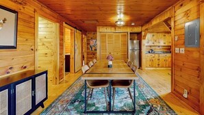 A wooden cabin interior with a dining table, chairs, a kitchen area, and a framed map on the wall. - Cozy house w/ mountain views, large yard, firepit, wifi, jetted tub, TV, EV (Glover)