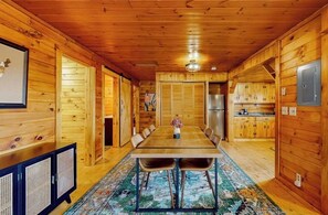 Interior de una cabaña de madera con una mesa de comedor, sillas, una zona de cocina y un mapa enmarcado en la pared.