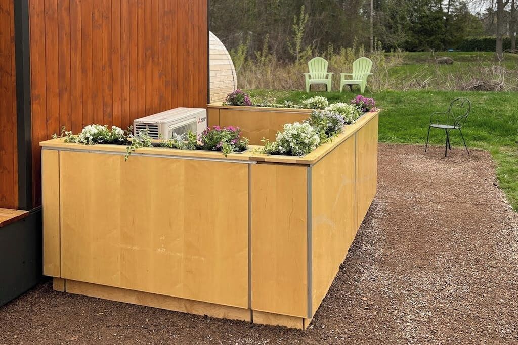 A wooden planter box with flowers, a green chair, and a small table in a garden setting.