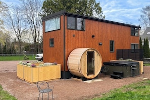 Ein modernes Holzhaus mit Sauna, einer Holzdiele und einer kleinen Sitzgelegenheit im Freien.