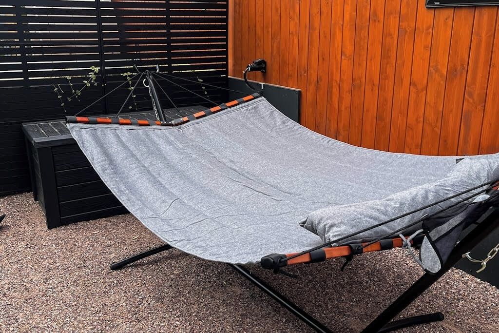 Een hangmat buiten, met een houten muur en een zwarte constructie op de achtergrond.