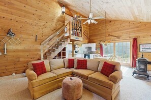 Ein Holzblockhaus-Innenraum mit Ecksofa, Deckenventilator, Treppe und Kaminofen.