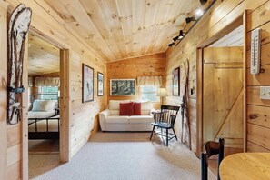 Ein gemütliches Holzblockhaus-Interieur mit einer Couch, Sesseln und einem Bett.