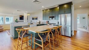 A modern kitchen with a central island, bar stools, and stainless steel appliances. - Lakefront house w/ views, beach, fireplace, firepit, central air, arcade games (Colchester)