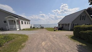 Une allée de gravier mène à une maison dotée d’un porche, d’une petite terrasse et offrant une vue sur l’eau.