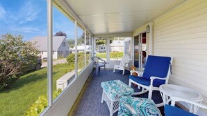 Une véranda avec vue sur un quartier résidentiel, des meubles en osier blancs et une petite table ronde.