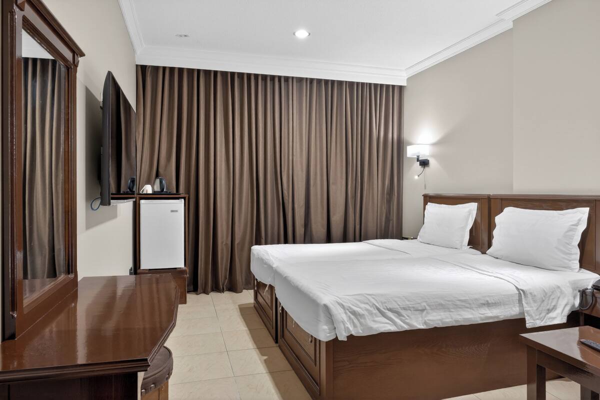 A hotel room with a bed, a desk, a television, and a wall-mounted light.