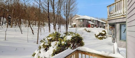 Ett bostadsområde med snötäckt mark, lövträd utan löv och ett hus med en synlig veranda.
