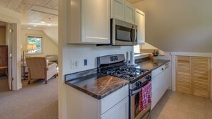 A kitchen with white cabinets, a gas stove, a microwave, and a red towel hanging on the oven.