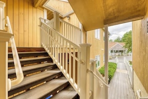 A wooden staircase with white railings leading to a covered porch. - Sleek condo with shared pool, tennis court, sauna, and hot tub (Stowe)