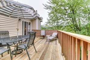 A wooden deck with a table and chairs, a striped umbrella, and a wooden railing. - Tranquil Retreat with Shared Pool, Hot Tub, and Private Deck - Close to Skiing (Stowe)