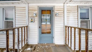 A two-story building with a blue door, white siding, and a wooden porch railing. - Cozy, Dog-Friendly Home w/ a Large Yard plus Free WiFi & a Private Washer/Dryer (Stowe)