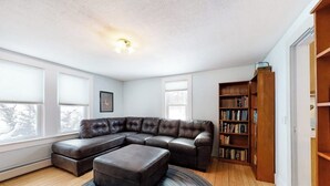 A living room with a sectional sofa, a small ottoman, a bookshelf, and a ceiling light fixture. - Cozy, Dog-Friendly Home w/ a Large Yard plus Free WiFi & a Private Washer/Dryer (Stowe)