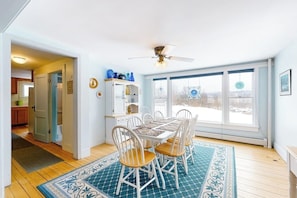 A dining area with a table and chairs, a ceiling fan, and a view through large windows. - Cozy, Dog-Friendly Home w/ a Large Yard plus Free WiFi & a Private Washer/Dryer (Stowe)