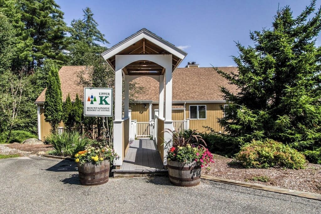 A mountain lodge entrance with a wooden porch, a sign indicating a 4K resort, and two flower planters.
