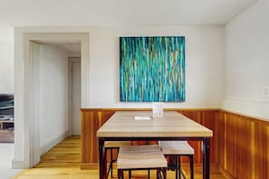 A dining area with a wooden table and benches, a wall-mounted abstract painting, and a wooden floor.