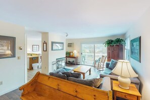 Ein Wohnzimmer mit einer Holzbank, einem Sofa, einem Couchtisch und einer Lampe. Es gibt einen Balkon mit Blick.