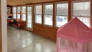 Una habitación con paredes de madera, ventanas amplias, una mesa con sillas y un dosel rosa.