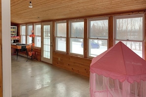 Ein Zimmer mit Holzwänden, großen Fenstern, einem Tisch mit Stühlen und einem rosafarbenen Baldachin.