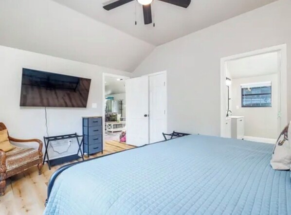 A bedroom with a large bed, a ceiling fan, a wardrobe, a desk, and a chair.
