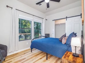 Un dormitorio con cama, escritorio, silla, ventana y ventilador de techo.