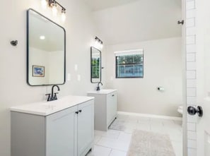 A bathroom with a white vanity, two mirrors, a window, and a shower area.