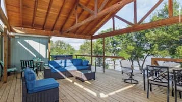 Una terraza exterior con piso de madera, un área techada con techo de madera y mobiliario que incluye sofás y sillones.
