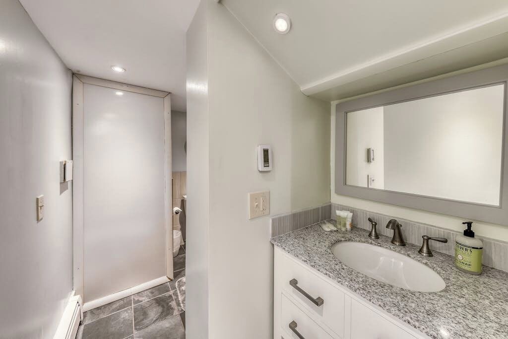 A bathroom with a white sink, a large mirror, and a door leading to another room.
