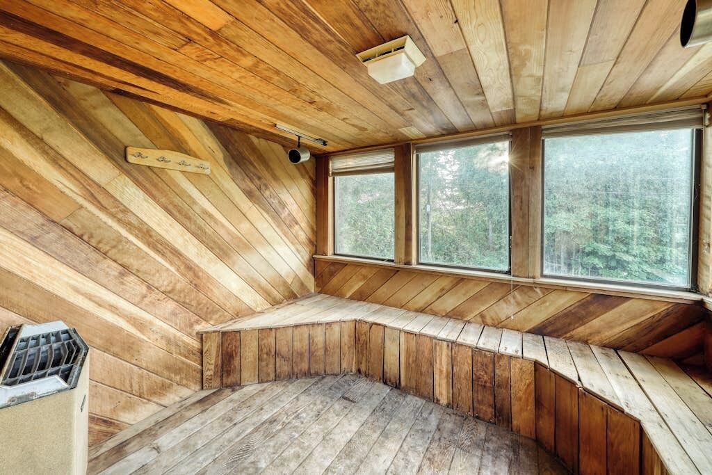 Interior d'una cabana de fusta amb una banca corbada, grans finestres i una sortida d'aire al sostre.